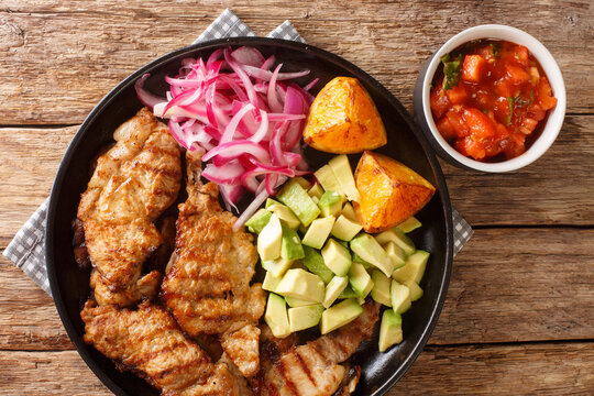 Poc chuc is a Mexican meat dish consisting of thin pork cutlets marinated in orange juice closeup in the plate on the table. Horizontal top view from above