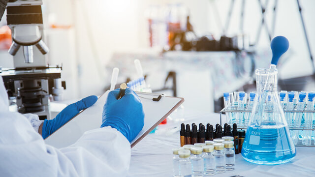 medical or scientific researcher researching and experimenting Multi-colored solution, vial and microscope In the laboratory or in the laboratory by wearing blue gloves and white clothing completely.