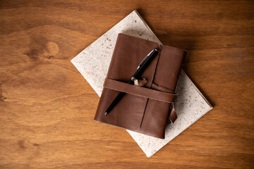 pencil and pens on a leather-covered blank sheet notebook on a recycled paper notebook on a wooden desk