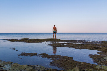 Young caucasian man in shorts, half body naked standing on Croatia sea shore edge. Back view