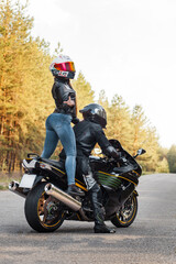 Motorcyclist in protective equipment and helmet shows fuck with a middle finger while sitting with a girl on a motorcycle