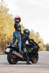Fototapeta na wymiar Motorcyclist in protective equipment and helmet shows fuck with a middle finger while sitting with a girl on a motorcycle