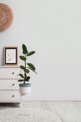 Modern chest of drawers with picture and houseplant near light wall