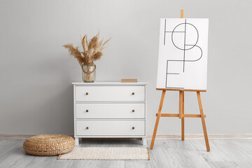Modern chest of drawers with vase and easel near light wall