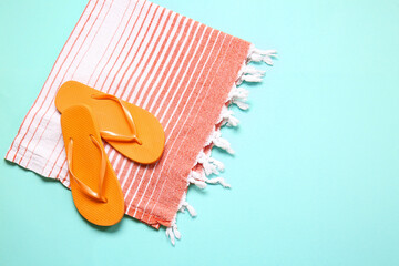 Stylish flip-flops and towel on color background