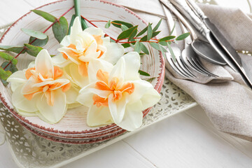 Beautiful table setting with narcissus flowers on light wooden background