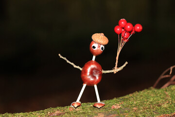 Funny crafted chestnut male with red balloons in front of black background standing on a mossy...