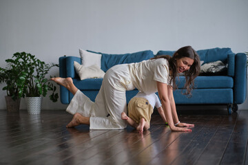 Happy mindful single mother doing morning exercises in yoga pose with kid playing at home. morning...