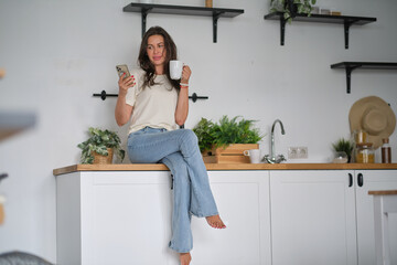 Young happy woman drinking coffee on the kitchen in the morning. Successful and confident female on a morning coffee break, resting and enjoying the drink.