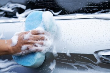 man washing black car with blue sponge
