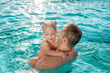 Father with baby daughter having fun on summer vacation splashing In outdoor swimming pool 