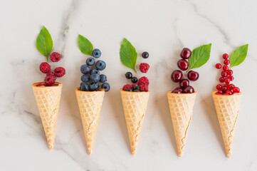 waffle cones with berries and mint leaves on a white marble table. delicious dessert. top view