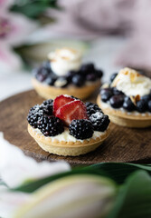 Tarts with blackberries and strawberries on wooden plate, close-up