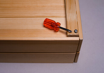 brown wooden box on a white background with a red phillips screwdriver background texture.the screwdriver is lying on a wooden box. the twisted screw is handmade. the box is handmade. wooden box with