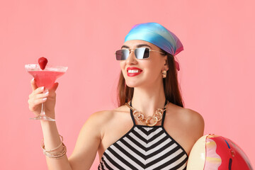 Beautiful young woman with cocktail and swimming ring on color background