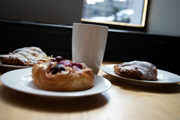 an almond croissant and a bun with strawberry slices lie on a white plate next to a white cup of coffee cappuccino and latte food fresh pastries bakery handmade kitchen cafe breakfast health