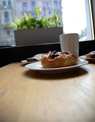 an almond croissant and a bun with strawberry slices lie on a white plate next to a white cup of coffee cappuccino and latte food fresh pastries bakery handmade kitchen cafe breakfast health