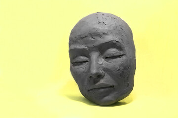 Fototapeta na wymiar Female face in clay on yellow background. Sculpture with Caucasian features, closed eyes, calm expression: in process of creation.