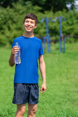 teenage boy exercising outdoors, sports ground in the yard, he opens a bottle of water and drinks, healthy lifestyle