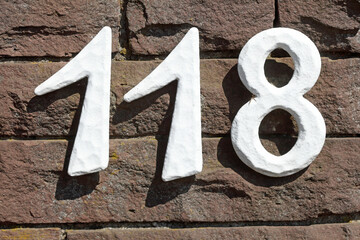 Weisses Hausnummernschild Nummer Hundertachtzehn auf einer dunklen Hausmauer, Deutschland, Europa