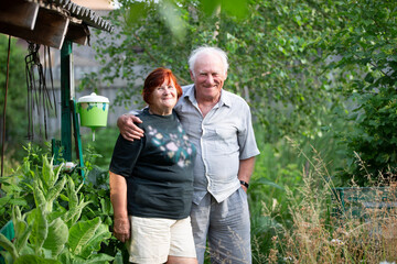 A beautiful very elderly couple hugs and looks at the camera at the dacha.