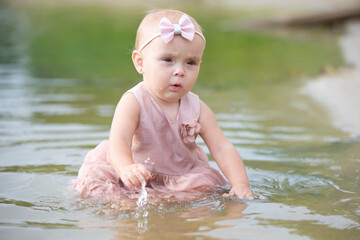 A beautiful little girl sits on the river bank and plays with sand and water. Child and nature.