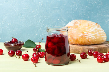 Jar of tasty cherry jam and bread on color background