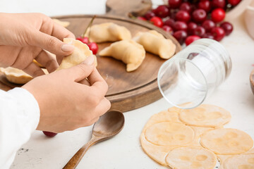 Woman preparing tasty cherry dumplings on table in kitchen, closeup