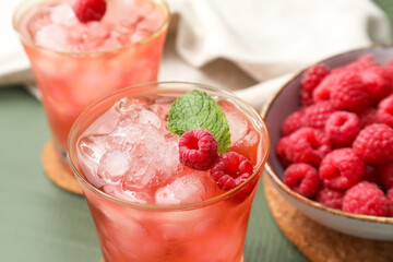 Glasses of tasty lemonade and bowl with raspberry on color wooden background