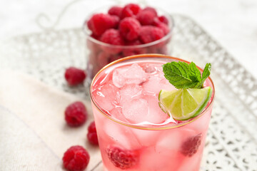Glass of tasty lemonade and bowl with raspberry on light background