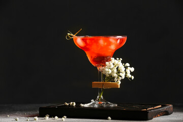 Glass with tasty cocktail and beautiful gypsophila flowers on dark background