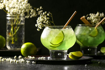 Glasses with tasty cocktail and beautiful gypsophila flowers on dark background