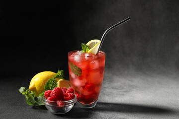 Glass of delicious lemonade, bowl with raspberry and lemon on dark background