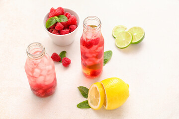 Bottles of delicious lemonade, bowl of raspberry and sliced lemon on light background