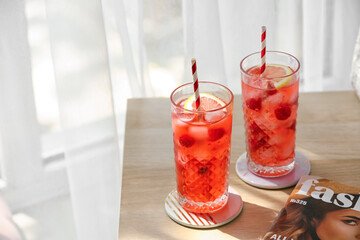 Glasses of cold raspberry lemonade on table near window