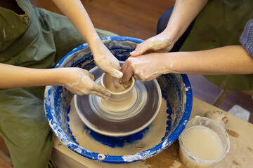 Close-up of a potter's hands and a child's hand with an item on a potter's wheel. Working with clay. Clay workshop. Craft training.