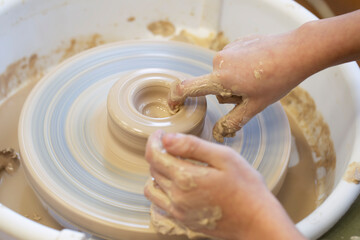 Close-up of a potter's hands with an item on a potter's wheel. Working with clay. Clay workshop. Craft training.