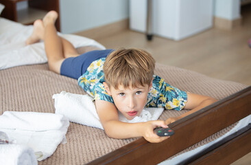 Fototapeta premium The child lies on the bed with the TV remote control.