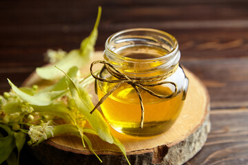 Honey in glass jar with linden flowers and wood slice on wooden table