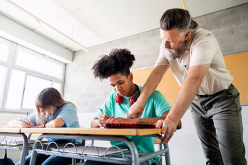 Caucasian mature man teacher with beard assisting black teenager boy high school student with...