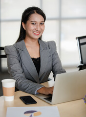 Young attractive Asian woman in grey business suit working on laptop in modern looking office. Concept for modern office lifestyle