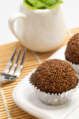 Perilla seed mixed with Jaggery palm sugar and mold into a ball place on a white plate decorated with mint leaves on a bamboo mat with spoons and forks.
