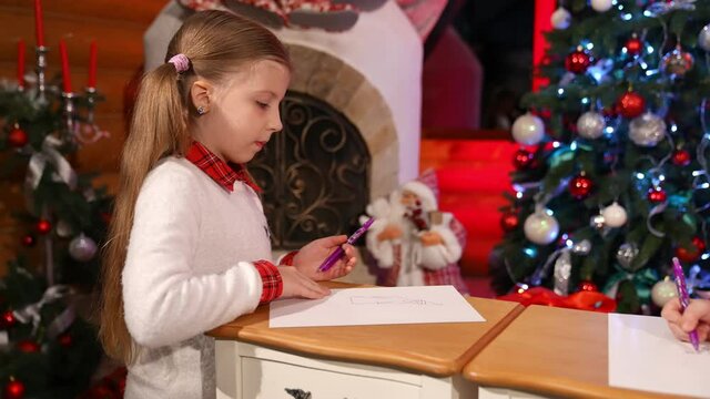 Children painting at Christmas decorated room. Cute little girls sitting on floor and drawing pictures on small desks for Santa. Christmas spirit concept
