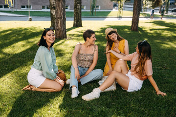 Group of four friends sitting in a park on green grass, having good time.