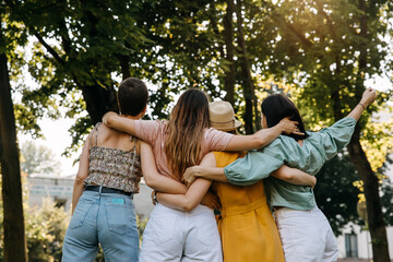 Four young teenage women friends, in a park, hugging together.