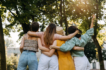 Group of four young women outdoors, hugging together from behind.