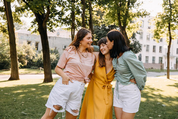 Group of three young women in a park, having good time, hugging and laughing.