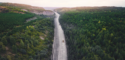 Large yellow truck rides through forest to be loaded into open coal mine