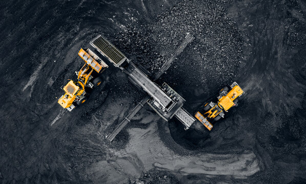 Yellow Excavator loads anthracite for crushing into coal crusher in open mine, aerial top view