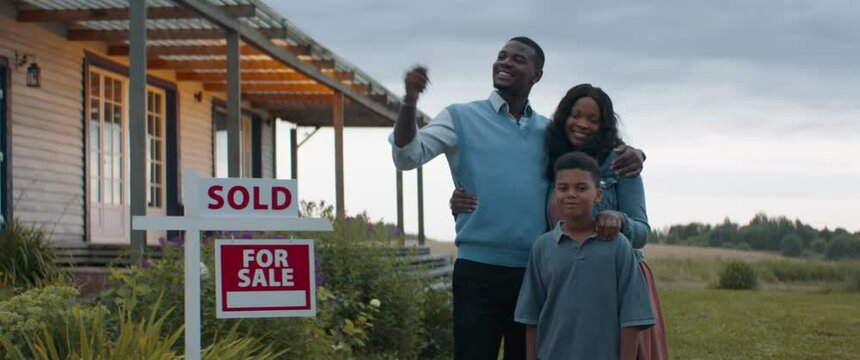 Portrait of happy African American Black family posing near sold sign, their new house in the background. Shot with 2x anamorphic lens